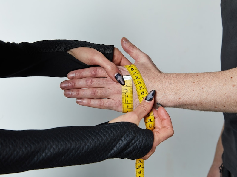 May include: A yellow measuring tape is being used to measure a person's wrist. The tape is wrapped around the wrist and the numbers on the tape are visible.