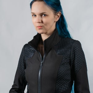 May include: A woman with blue hair wearing a black zippered jacket with a textured design.