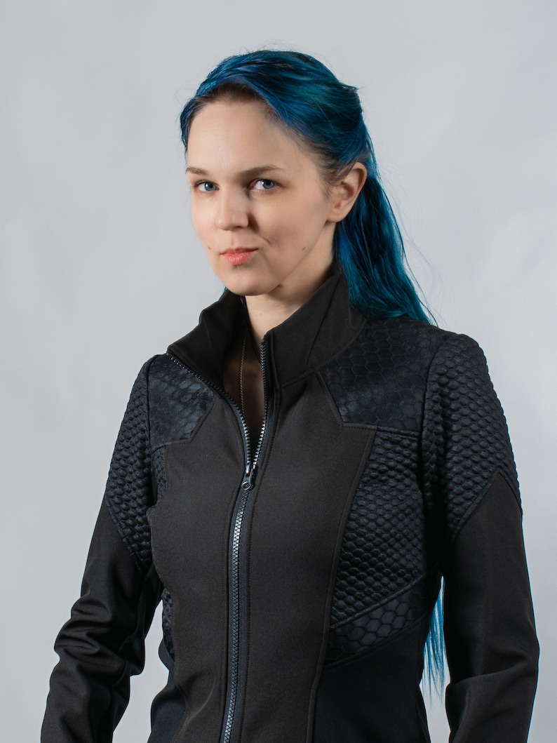 May include: A woman with blue hair wearing a black zippered jacket with a textured design.