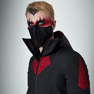May include: A black face mask with a quilted texture and a black hooded jacket featuring red textured panels on the chest and shoulders. The jacket has a high collar, a front zipper, and quilted detailing on the sleeves and upper chest area.