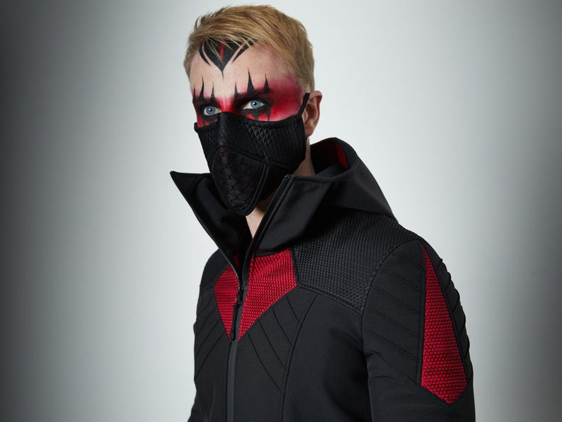 May include: A black face mask with a quilted texture and a black hooded jacket featuring red textured panels on the chest and shoulders. The jacket has a high collar, a front zipper, and quilted detailing on the sleeves and upper chest area.