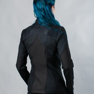 May include: Black quilted jacket with a star-shaped design on the back. The jacket has a zipper closure and long sleeves.