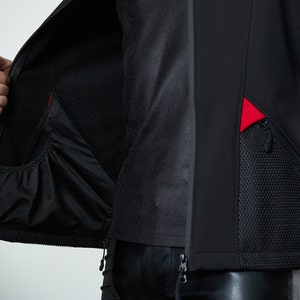May include: A black jacket featuring a full-length front zipper, a smooth exterior finish, and an interior pocket with an elasticized opening. The exterior includes a textured mesh pocket panel accented with vibrant red fabric inserts.