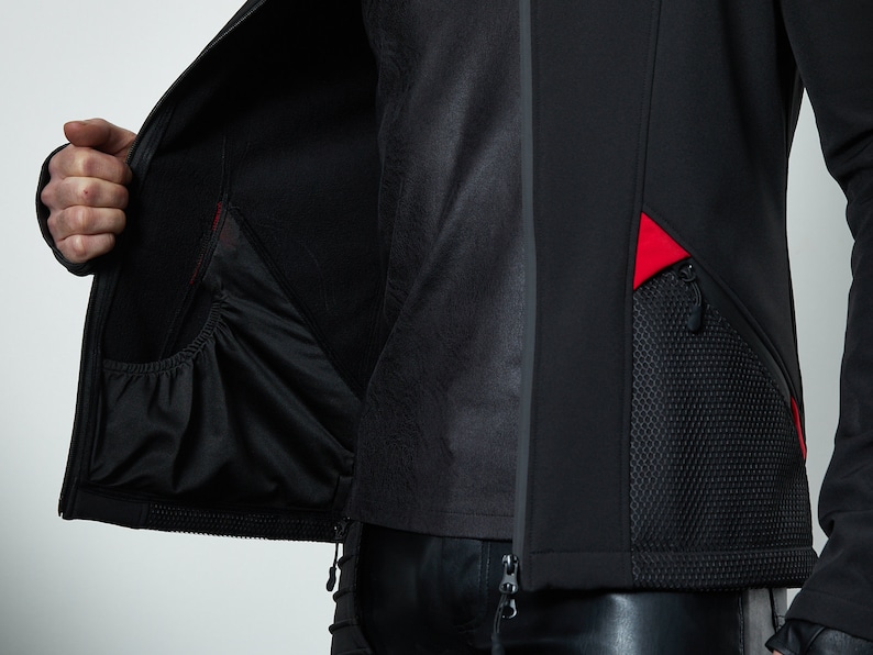 May include: A black jacket featuring a full-length front zipper, a smooth exterior finish, and an interior pocket with an elasticized opening. The exterior includes a textured mesh pocket panel accented with vibrant red fabric inserts.