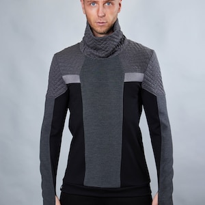 Op de afbeelding: Een zwart longsleeve shirt met een hoge mock neck kraag en een gewatteerd ontwerp op de schouders en mouwen. Het shirt heeft een zwart-grijs gestreept paneel aan de voorkant.