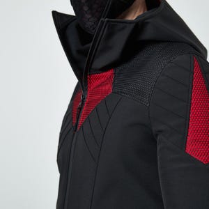 May include: A black hooded jacket featuring a high collar and a front zipper. The garment includes red hexagonal mesh panels on the chest and shoulders, complemented by black quilted stitching details across the sleeves and upper torso area.