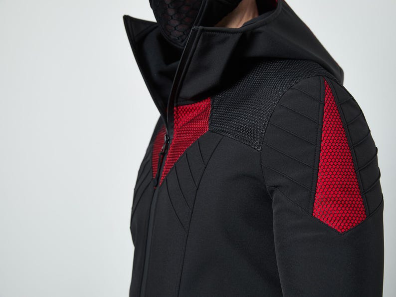 May include: A black hooded jacket featuring a high collar and a front zipper. The garment includes red hexagonal mesh panels on the chest and shoulders, complemented by black quilted stitching details across the sleeves and upper torso area.