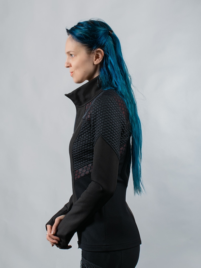 May include: A black zippered jacket with a mesh panel on the side. The jacket has a stand-up collar and long sleeves. The model has blue hair.
