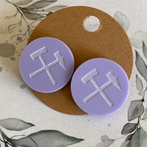 Könnte beinhalten: Ein Paar runde Ohrringe in Lavendelfarbe mit einem weißen Hammer- und Pfeil-Design. Die Ohrringe haben eine glatte, matte Oberfläche.