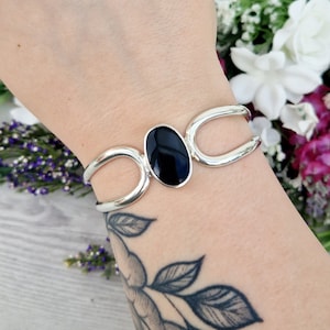 May include: A silver bracelet with a black oval gemstone. The bracelet has a simple, elegant design and is perfect for everyday wear.