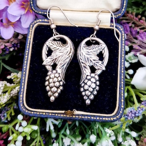 May include: A pair of silver earrings with a grape cluster design. The earrings are in a blue velvet box with gold trim.