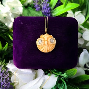 May include: A gold chain necklace with a carved ivory pendant featuring two small diamond accents. The pendant is shaped like an owl with its eyes made of diamonds. The necklace is displayed in a purple velvet box.