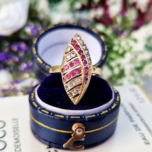 Puede incluir: Un anillo de oro con un diseño en forma de hoja engastado con piedras rosas y blancas. El anillo se muestra en una caja de anillo de terciopelo azul.