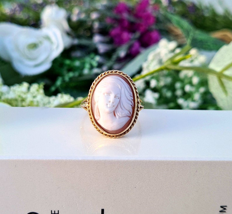Op de afbeelding: Een gouden ring met een cameo met een gegraveerd portret van een vrouw met lang haar. De cameo is gezet in een ovale gouden lijst.