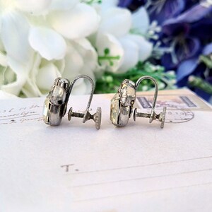 May include: A pair of silver clip-on earrings with clear rhinestone accents. The earrings have a screw-back closure.