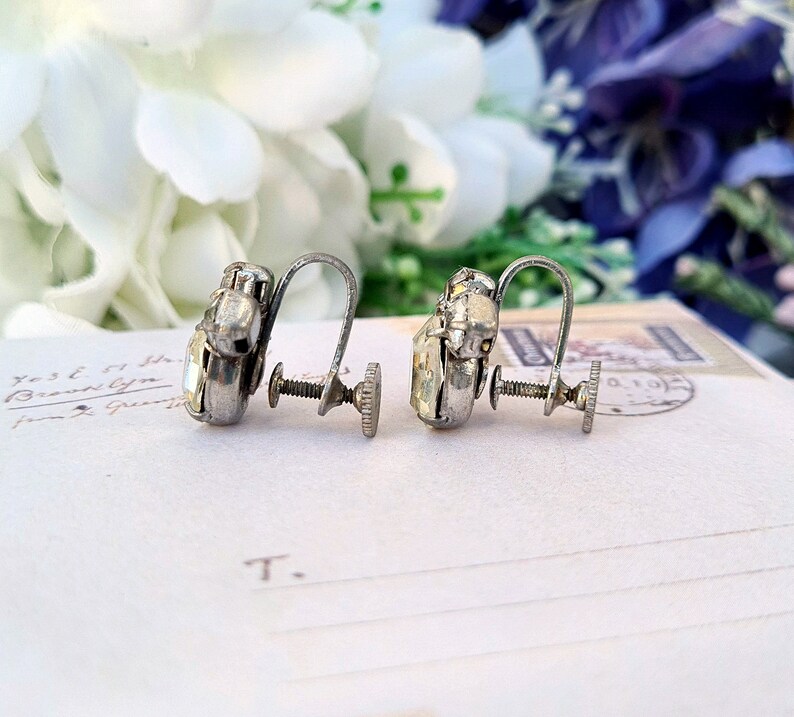 May include: A pair of silver clip-on earrings with clear rhinestone accents. The earrings have a screw-back closure.