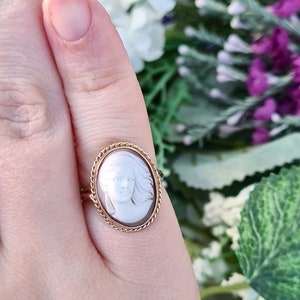 Op de afbeelding: Een gouden ring met een cameo met het profiel van een vrouw in wit op een bruine achtergrond.