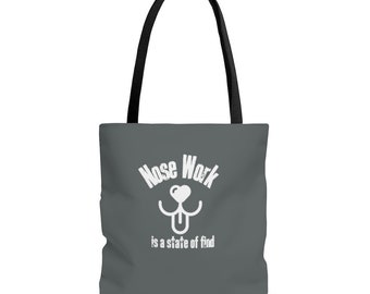 May include: A gray tote bag with black handles. The bag has a white graphic of a dog's nose with the text "Nose Work is a state of find".