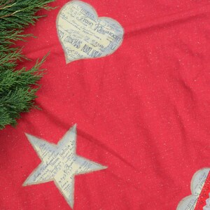 May include: Red Christmas tree skirt with a white star and heart design. The skirt has a white lace trim.