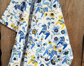 May include: A white tea towel with a blue and yellow floral pattern featuring stylized horses. The horses are a traditional Swedish folk art design.