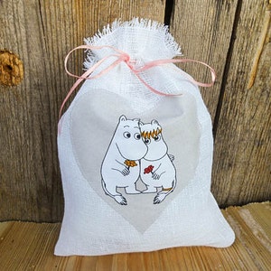 May include: A white linen drawstring bag with a pink ribbon and a heart-shaped window featuring a black and white illustration of two cartoon characters holding a flower.