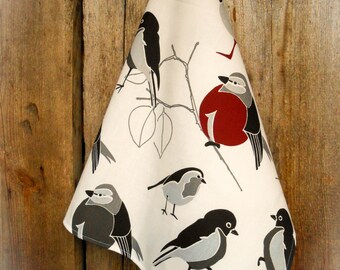 Puede incluir: Un paño de cocina blanco con un diseño de pájaros negro y gris. Los pájaros están posados en ramas con bayas rojas. El paño está colgado en una pared de madera.