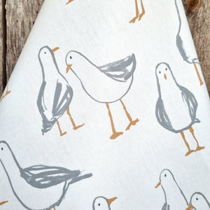 Puede incluir: Tela blanca con un patr&oacute;n repetido de gaviotas estilizadas en gris y beige. Las gaviotas est&aacute;n representadas en un estilo simple e ilustrativo, con contornos grises y detalles beige.