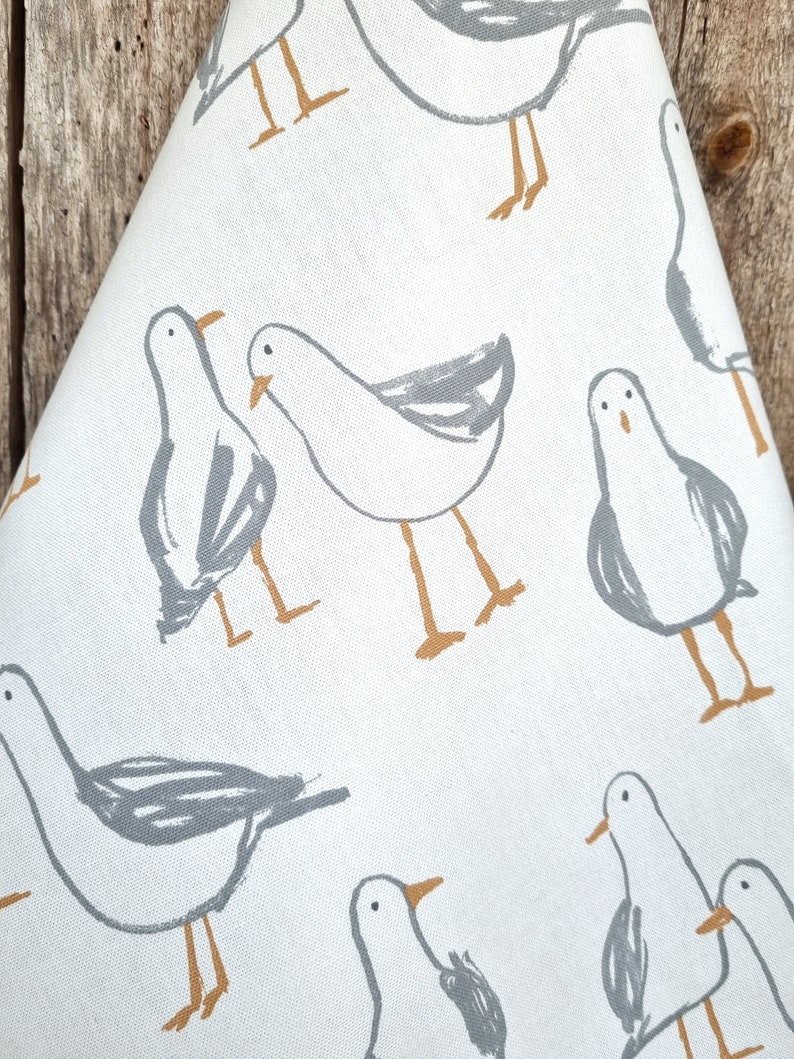 Puede incluir: Tela blanca con un patr&oacute;n repetido de gaviotas estilizadas en gris y beige. Las gaviotas est&aacute;n representadas en un estilo simple e ilustrativo, con contornos grises y detalles beige.