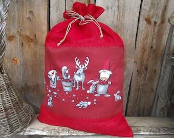May include: A red fabric gift bag with a drawstring closure. The bag features a whimsical print of gnomes, a deer, squirrels, and rabbits gathering red berries. The bag has a decorative scalloped edge.