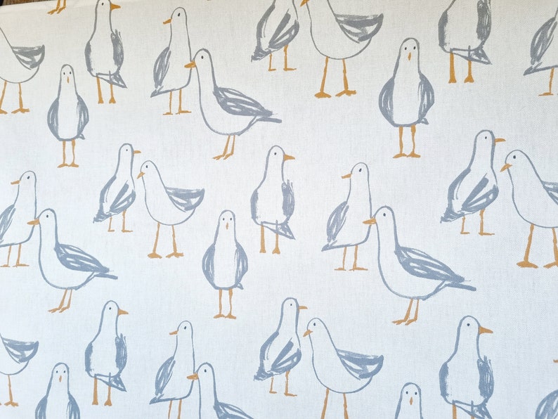 Puede incluir: Tela blanca con un patr&oacute;n repetido de gaviotas esbozadas en gris y beige. Las gaviotas se representan en varias poses, algunas de pie y otras en parejas, creando un tema costero caprichoso.