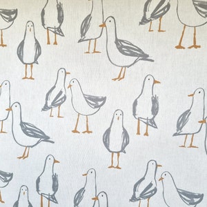 Puede incluir: Tela blanquecina con un patr&oacute;n repetido de gaviotas grises estilizadas con patas y picos naranjas. Las gaviotas est&aacute;n en varias poses, creando un dise&ntilde;o caprichoso y n&aacute;utico. La tela parece ser de algod&oacute;n o lino.