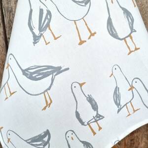 Puede incluir: Tela blanca con un patr&oacute;n repetido de gaviotas estilizadas en gris y marr&oacute;n. Las gaviotas est&aacute;n representadas con dibujos de l&iacute;neas simples, y la tela tiene un aspecto ligeramente texturizado. El dise&ntilde;o evoca un tema costero.