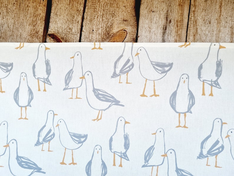 Puede incluir: Tela blanca con un patr&oacute;n repetido de gaviotas de dibujos animados en gris y beige. Las gaviotas est&aacute;n dibujadas con l&iacute;neas y formas simples, lo que les da una apariencia caprichosa. El fondo es de color crema claro.