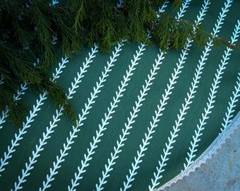 Puede incluir: Un mantel verde con un patrón de hojas blancas y un borde de encaje blanco. El mantel está hecho de una tela suave y texturizada.