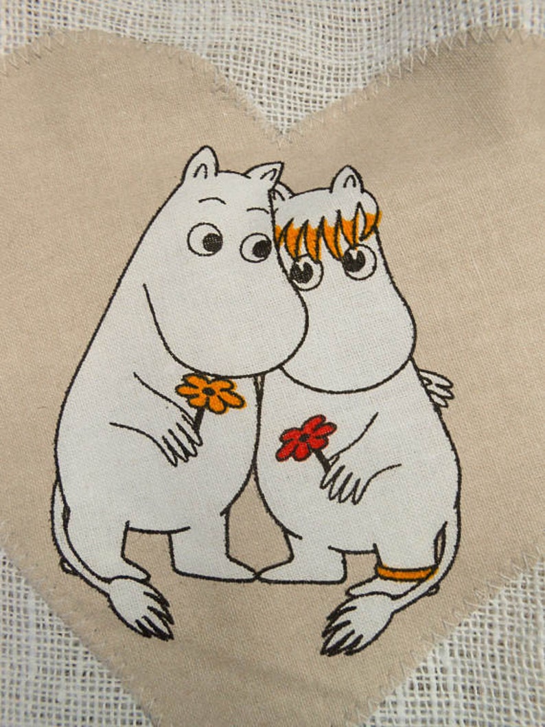 May include: Two white cartoon characters with black outlines and orange and red flowers are hugging on a beige fabric background. The characters have large black eyes and are holding flowers.