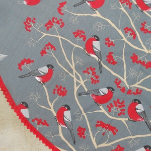 May include: A gray and white fabric with a repeating pattern of red berries and black and white birds. The birds are perched on branches with red berries.