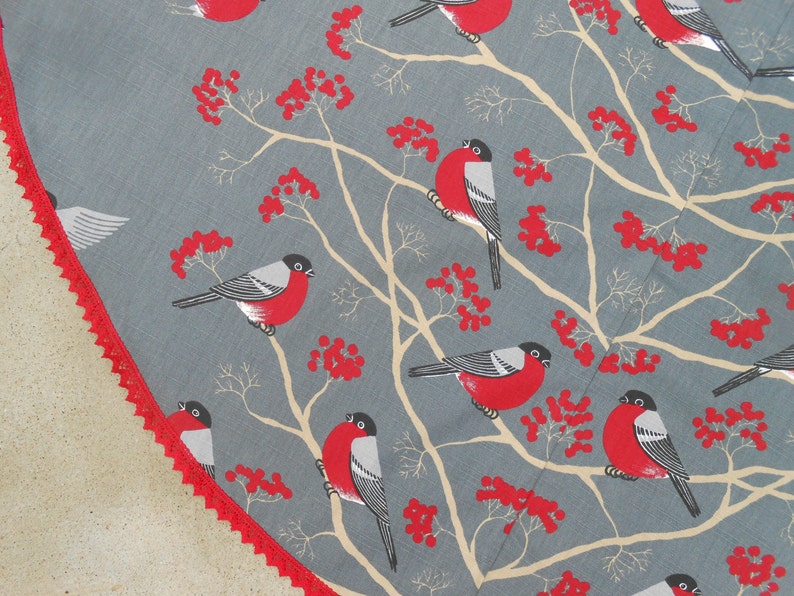 May include: A gray and white fabric with a repeating pattern of red berries and black and white birds. The birds are perched on branches with red berries.