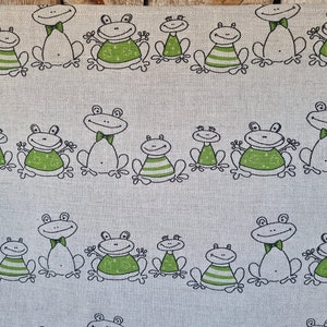 Puede incluir: Una tela blanca con un patr&oacute;n repetido de ranas verdes. Las ranas est&aacute;n dibujadas en un estilo de dibujos animados simple con contornos negros. Algunas ranas llevan pajaritas.