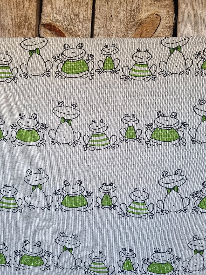 Puede incluir: Una tela blanca con un patr&oacute;n repetido de ranas verdes. Las ranas est&aacute;n dibujadas en un estilo de dibujos animados simple con contornos negros. Algunas ranas llevan pajaritas.