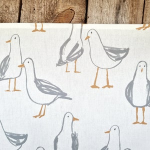 Puede incluir: Tela blanca con un estampado repetido de gaviotas de dibujos animados en gris y marr&oacute;n. Las gaviotas est&aacute;n representadas en varias poses. La tela tiene una textura similar a la del lino, ideal para la decoraci&oacute;n del hogar.