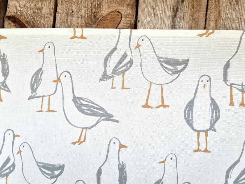 Puede incluir: Tela blanca con un estampado repetido de gaviotas de dibujos animados en gris y marr&oacute;n. Las gaviotas est&aacute;n representadas en varias poses. La tela tiene una textura similar a la del lino, ideal para la decoraci&oacute;n del hogar.