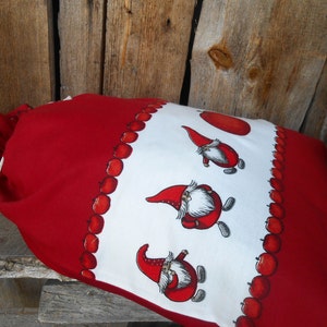May include: Red and white fabric bag with a drawstring closure. The bag is decorated with a pattern of red apples and gnomes.
