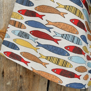 Peut inclure: Une serviette de cuisine en tissu blanc avec un motif coloré de poissons stylisés. Les poissons sont dans des tons de rouge, orange, jaune, bleu et vert. Les poissons sont disposés de manière aléatoire.