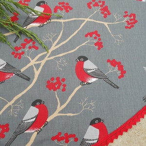May include: A gray fabric tablecloth with a red trim and a repeating pattern of red berries and black and red birds.