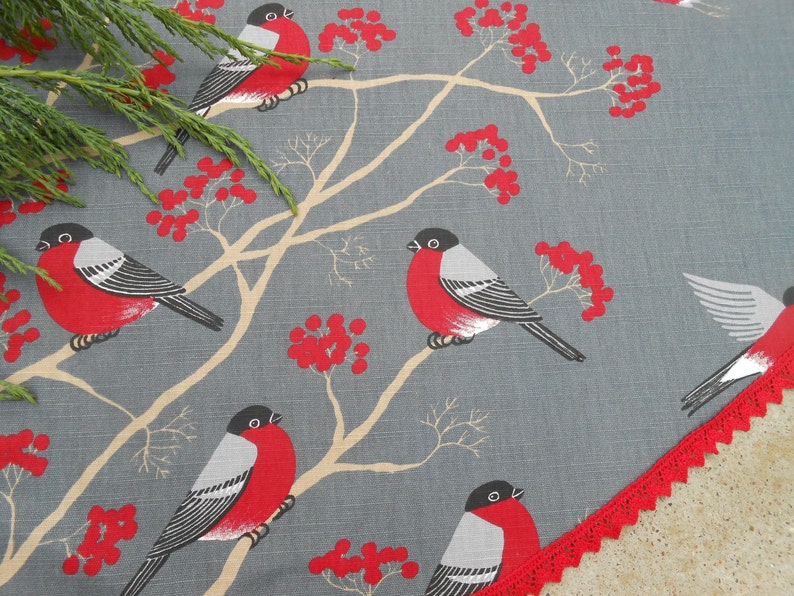 May include: A gray fabric tablecloth with a red trim and a repeating pattern of red berries and black and red birds.