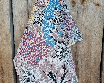 Puede incluir: Un paño de cocina blanco con un patrón floral en tonos marrones, azules, amarillos y rosas. El paño está colgado en una superficie de madera.