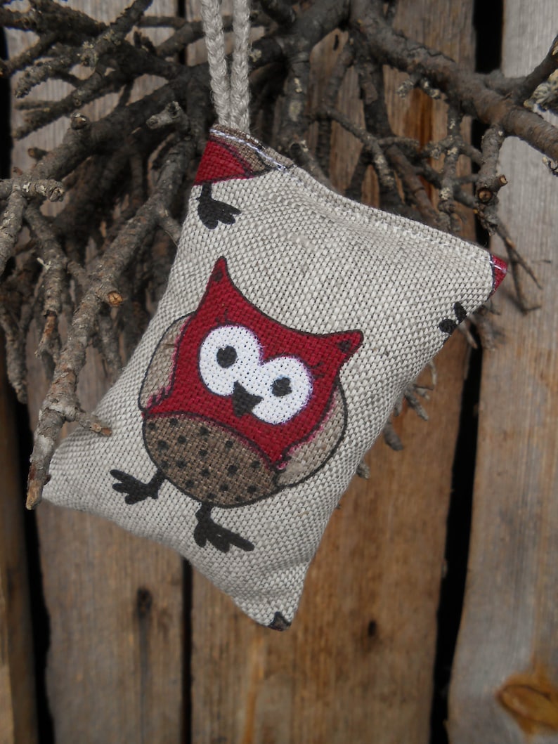 May include: A small, beige fabric pouch with a red owl design. The owl has black eyes and a white beak. The pouch is hanging from a brown string.