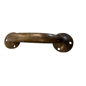 May include: A dark bronze-toned metal door handle featuring a curved grip and two circular mounting plates at each end. Each mounting plate contains two pre-drilled holes for installation. The metal surface displays a weathered, textured finish.