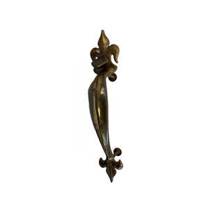 May include: A vertical brass door handle featuring a polished metallic finish and a curved, elongated body. The handle is anchored at both the top and bottom by decorative fleur-de-lis motifs, providing a symmetrical design for door operation.