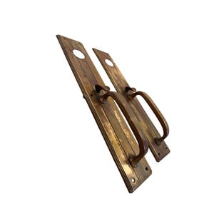 May include: Two antique brass door handles with a rectangular backplate and a curved handle. The handles have a weathered, aged appearance, with visible wear and tear. Each backplate has a circular hole near the top.